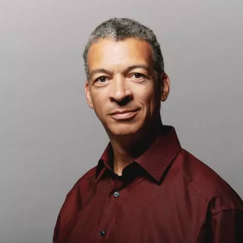 Man in burgundy shirt with neutral expression looking towards the camera