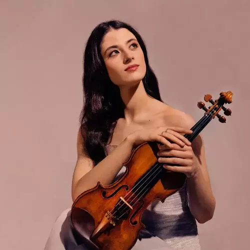 Woman with brown hair looks up into the sky while holding a violin in front of pink background