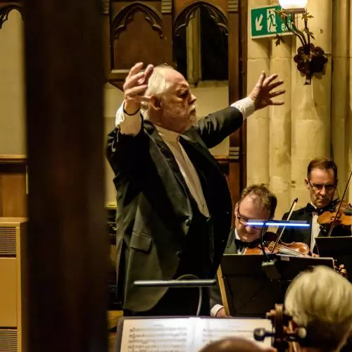 Conductor in a suit with his arms open to an orchestra